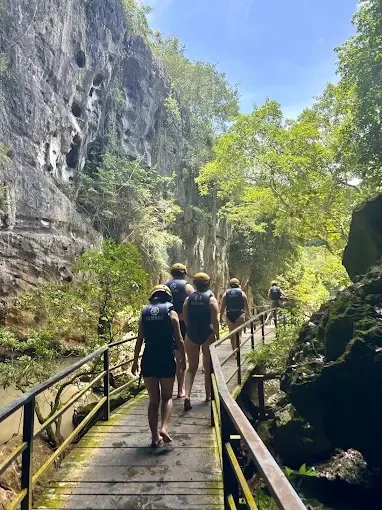A group in helmets and life jackets walking the boardwalk through the gorge to Dark Cave