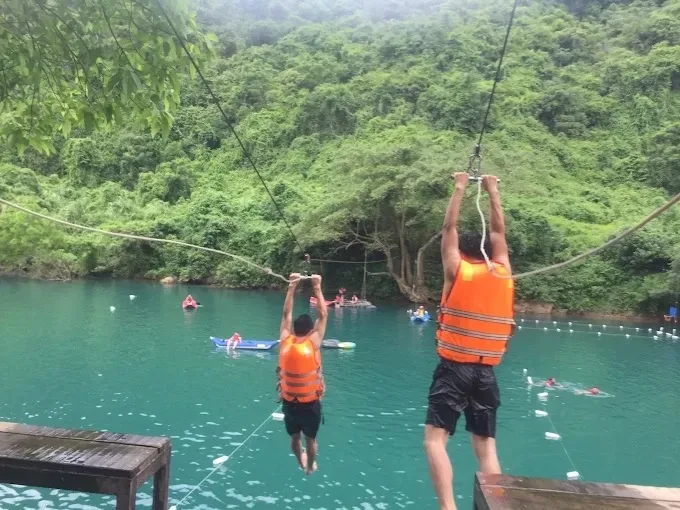 Two people on the zipline across the turquoise Chay River towards Dark Cave