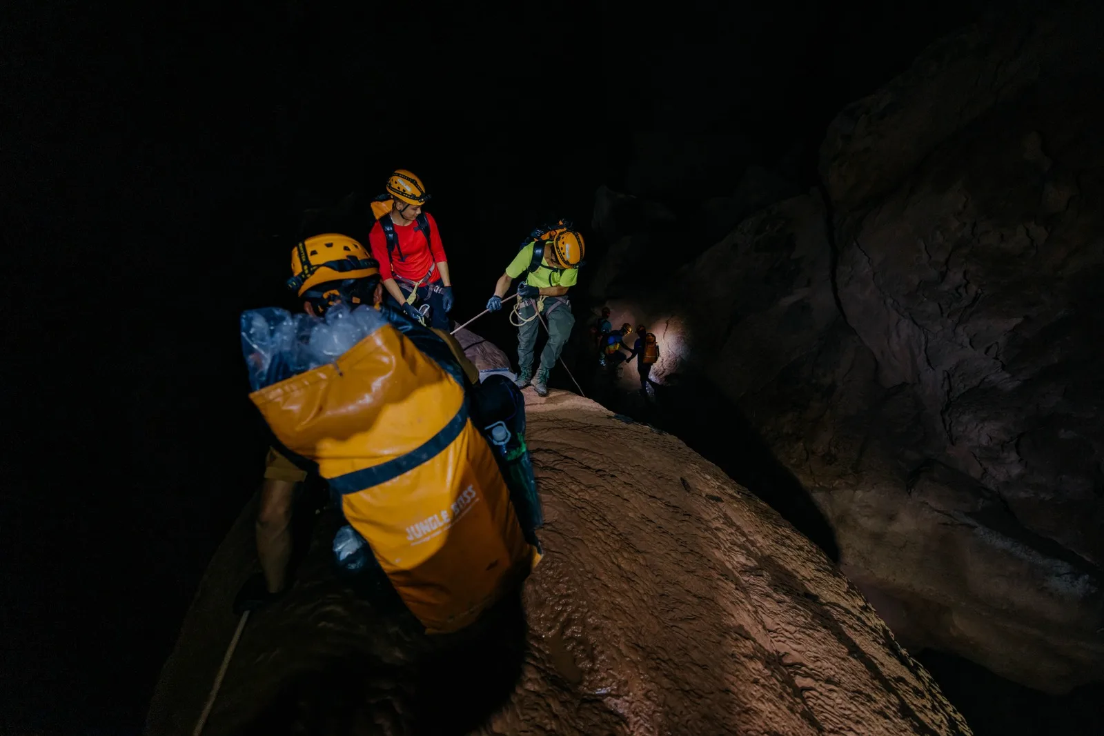Cavers hauling a yellow dry bag over boulders inside Hang Pygmy
