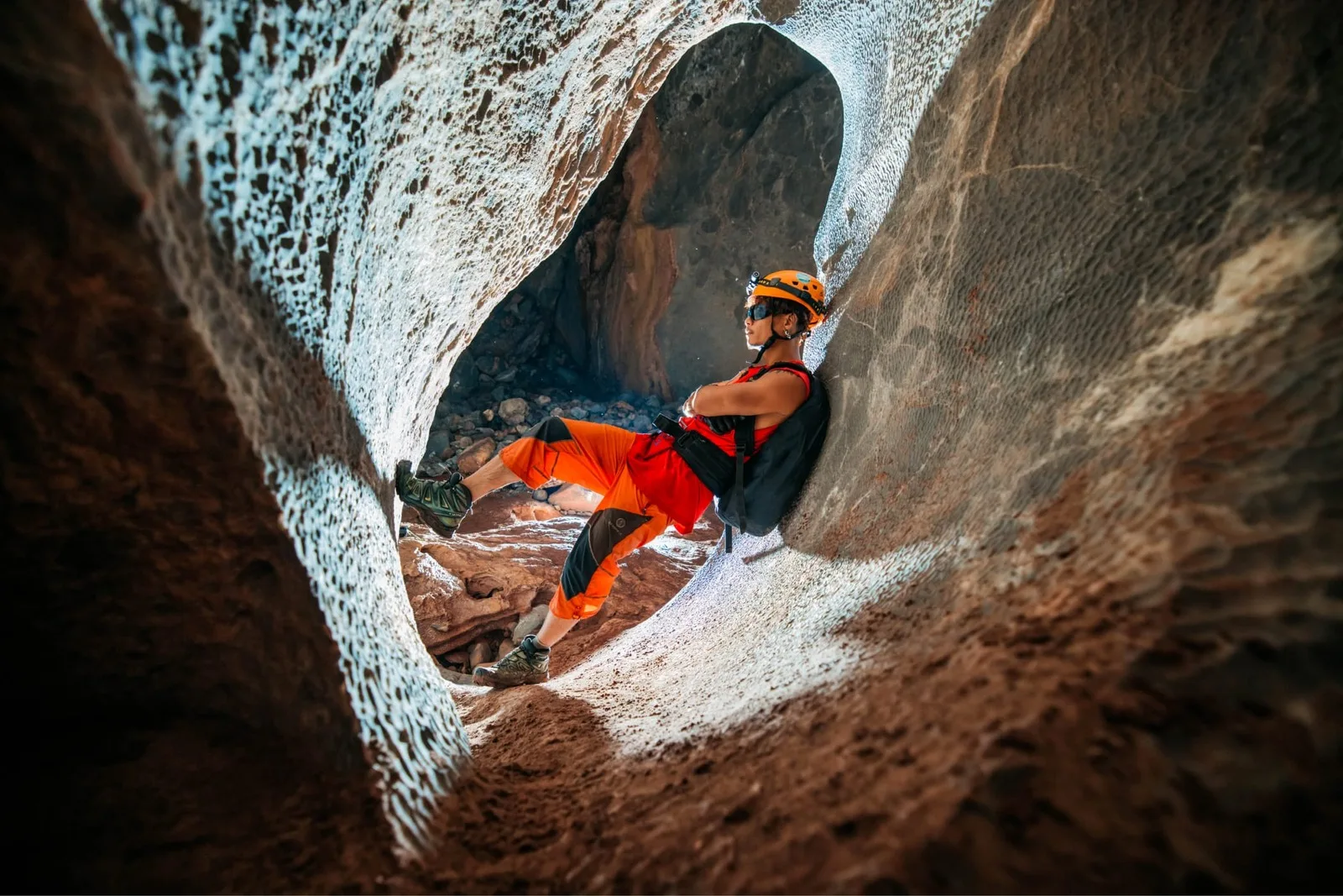 A caver in orange working through a narrow rock section on the Kong Collapse trip