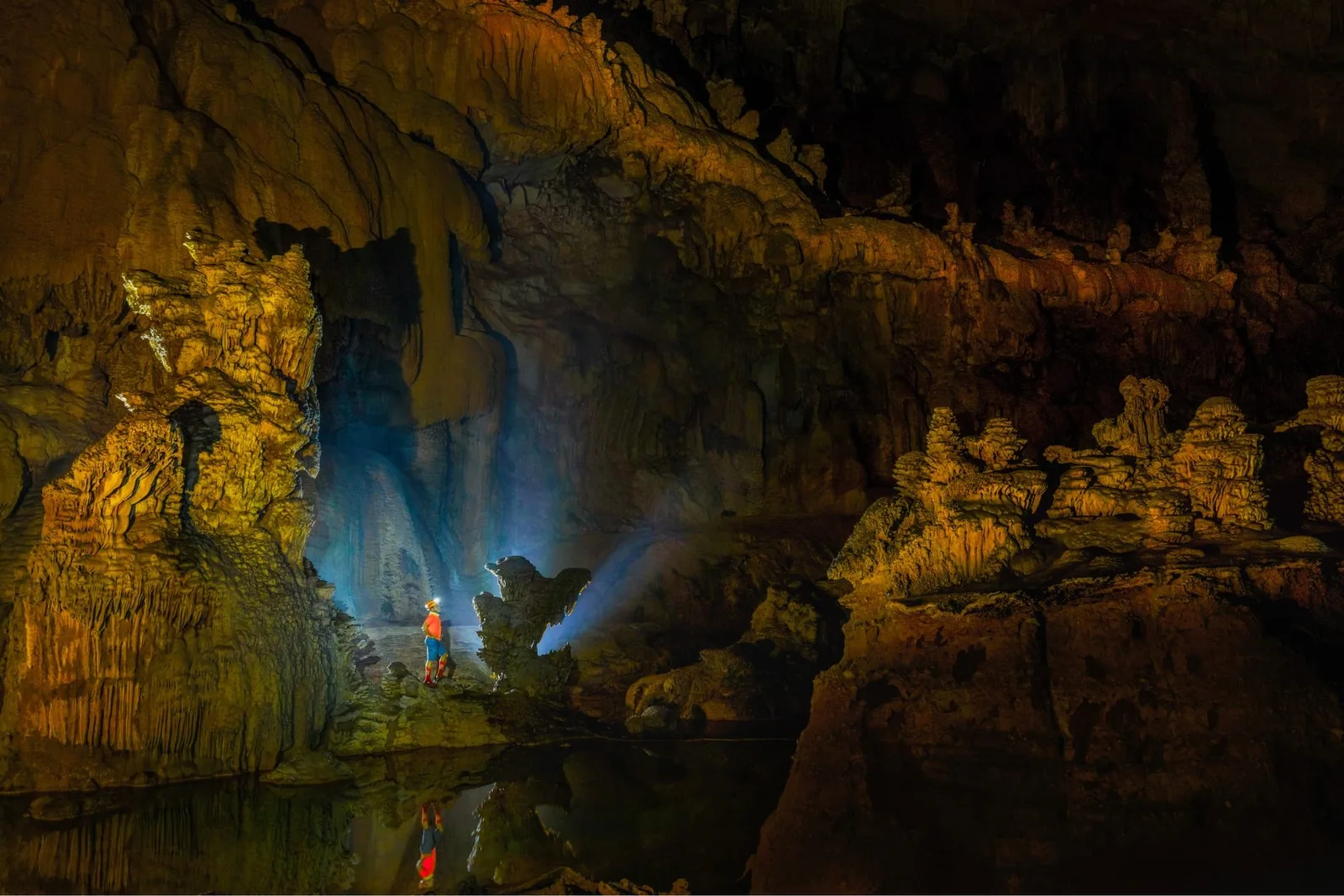 A caver walking a wide golden-walled passage inside Tiger Cave