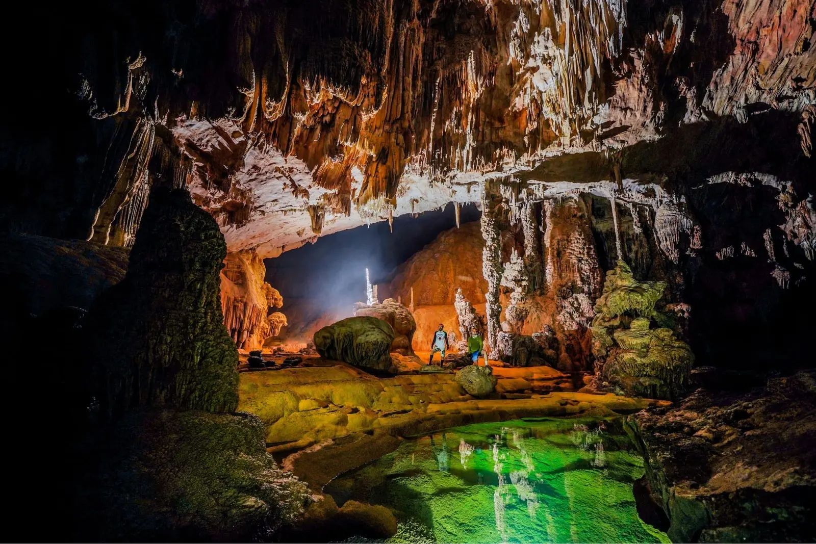 A lit green pool beneath stalactites in the Tiger Cave system